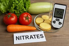 На столі лежать свіжі овочі — помідори, морква, листя салату та кабачок. Поруч розрізана картопля і електронний прилад для вимірювання нітратів, який показує значення «350». На передньому плані напис «NITRATES».
