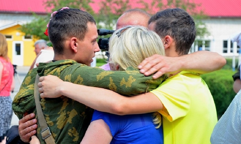 Фото на якому зображено як люди у цивільному одязі обіймають військового.