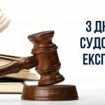 Дерев'яний молоток судді та відкрита книга на білому фоні з написом "З Днем судового експерта