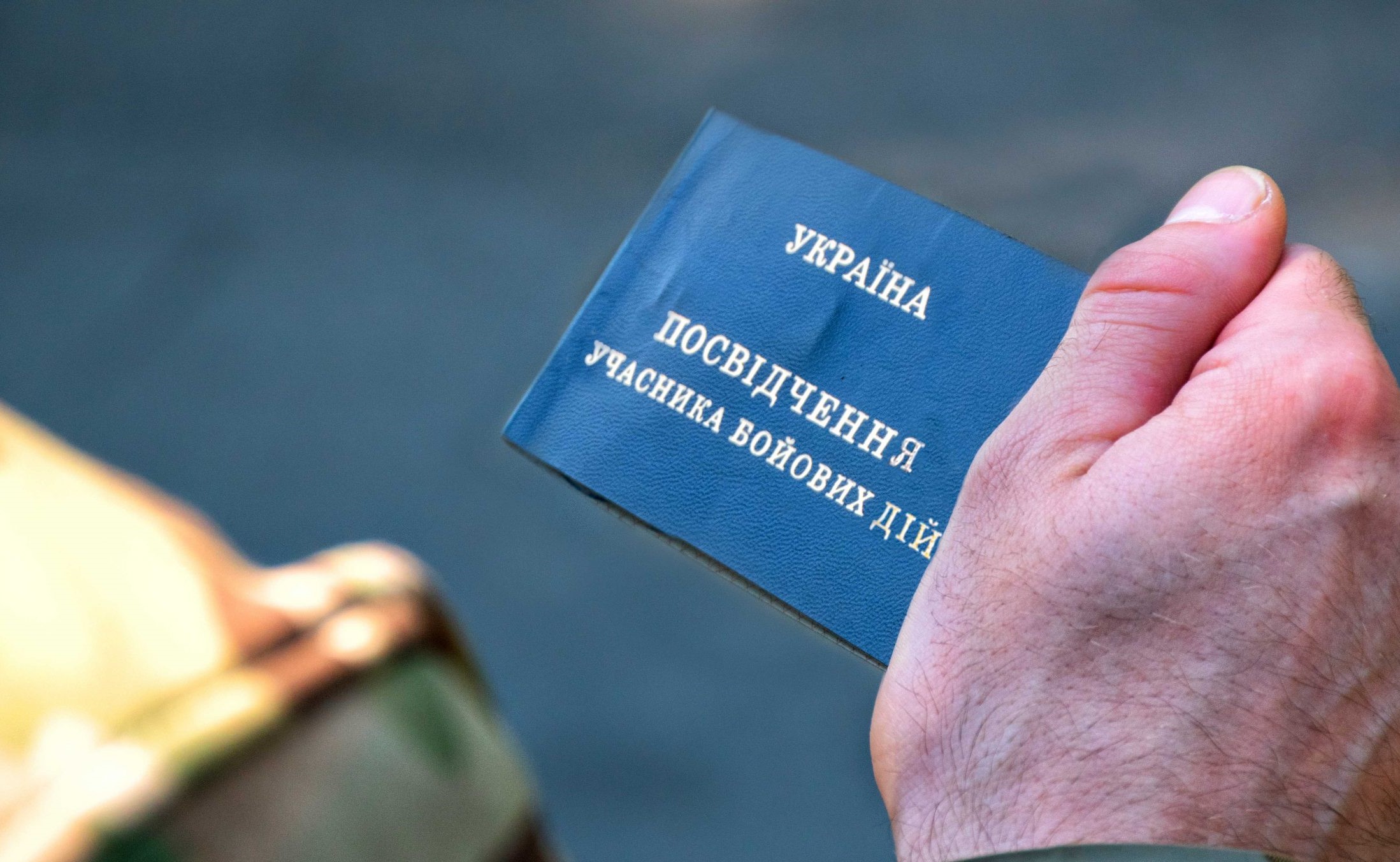 Рука тримає синє посвідчення учасника бойових дій від України