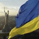 Український прапор майорить на вітрі, на задньому плані видно монумент Батьківщина-Мати в Києві