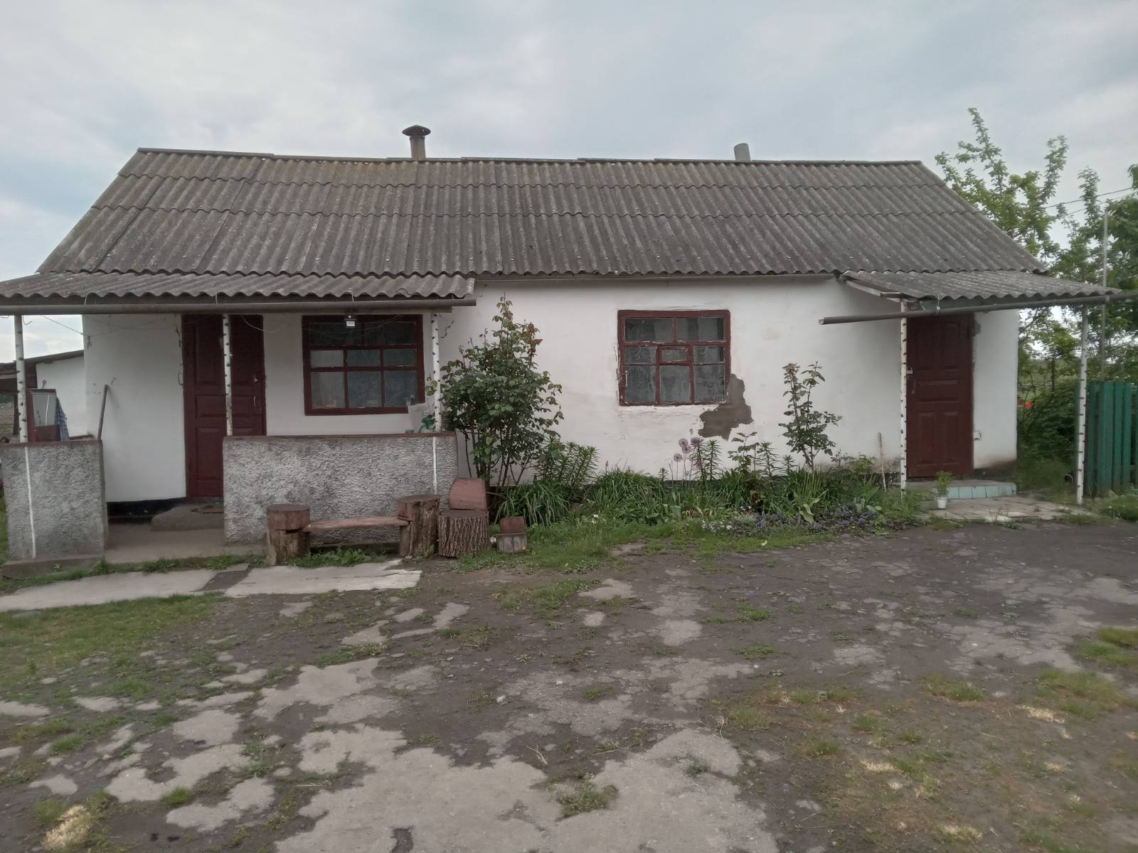 Невеликий сільський будинок з білими стінами, сірим хвилястим дахом, двома вікнами та дверима.