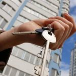 Рука тримає ключі від квартири на тлі багатоповерхових житлових будинків