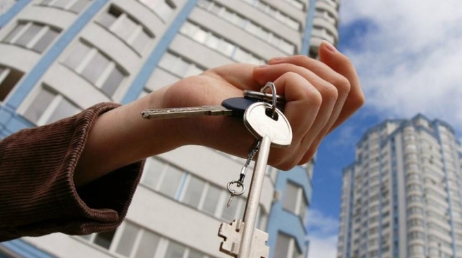 Рука тримає ключі від квартири на тлі багатоповерхових житлових будинків