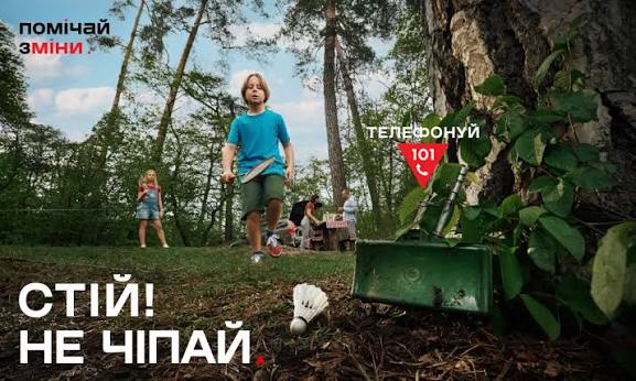 Дитина з бадмінтоном помічає небезпечний предмет на землі серед лісу. Напис: «Стій! Не чіпай. Телефонуй 101»
