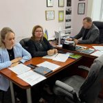 Троє людей сидять за довгим столом в офісі під час наради